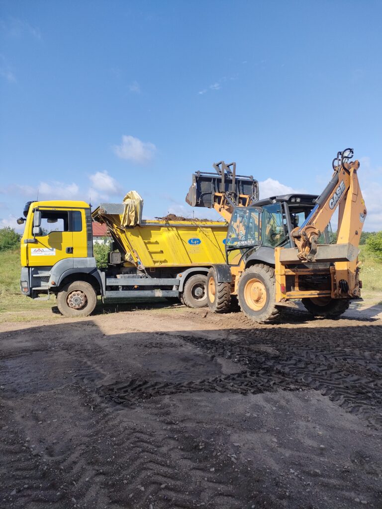 Koparko-ładowarka Case podczas załadunku żółtej wywrotki MAN na placu budowy, świadcząca usługi ziemne i transportowe dla firmy Walenda Usługi Sprzętowe w Suwałkach.
