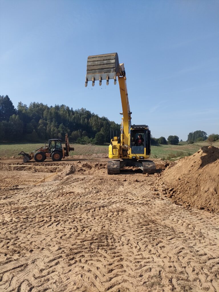 Żółta koparka w trakcie prac ziemnych na placu budowy, świadcząca usługi dla firmy Walenda Usługi Sprzętowe w Suwałkach i okolicach.