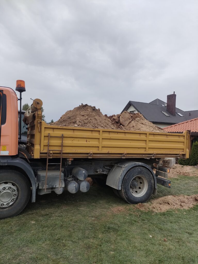 Wywrotka załadowana ziemią podczas prac budowlanych na terenie mieszkalnym, świadcząca usługi transportowe dla firmy Walenda Usługi Sprzętowe w Suwałkach.