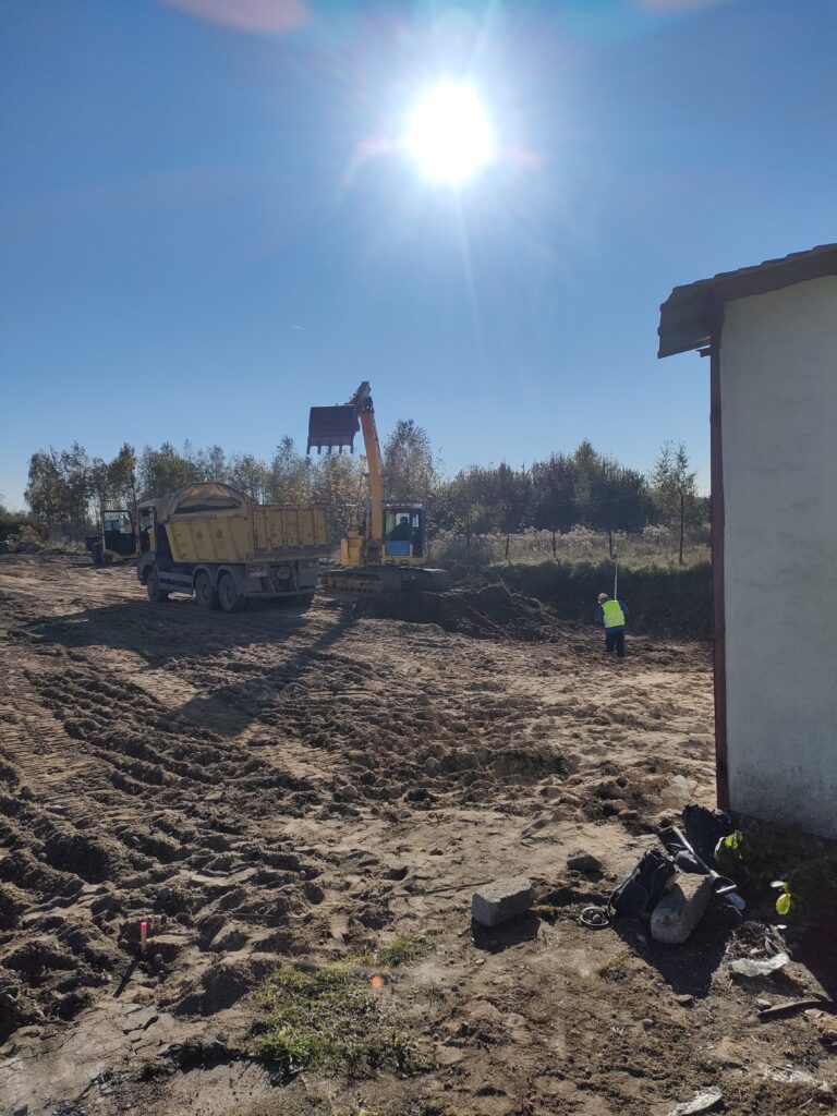 Koparka załadowująca ziemię na żółtą wywrotkę podczas prac ziemnych na placu budowy w słoneczny dzień, świadcząc usługi dla firmy Walenda Usługi Sprzętowe w Suwałkach.